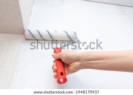 Applying primer and glue with a wide roller on the plastered surface of the wall for wallpapering Royalty-Free Stock Photo #1948170937