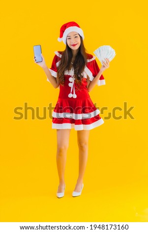 Portrait beautiful young asian woman wear christmas clothes and hat with cash and money on yellow isolated background