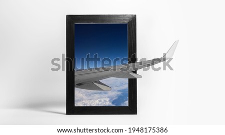 Artwork collage concept. View of wing of flying airplane in the sky through black wooden frame on white background.