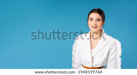 Banner, long format. Surprised business woman in white office clothes against blue studio background with empty side ad space. Success of young entrepreneurs. High quality photo