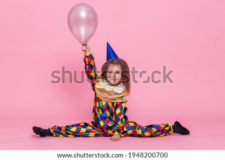 portrait little girl in a clown costume sits on a twine on a pink background
