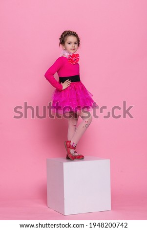 happy laughing little long hair girl dancing on pink background. little girl on a white cube on a pink background