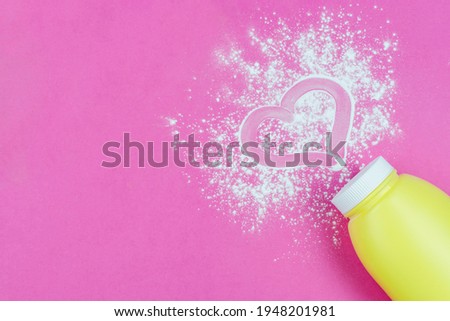 Scattered children powder under a diaper from a yellow bottle on a bright pink background. A drawing of a heart made with a finger on the powder. Space for the text. Love for your baby. Royalty-Free Stock Photo #1948201981