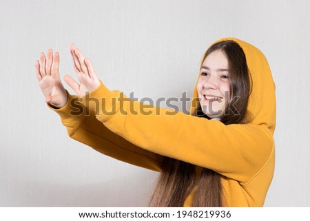 The teenage girl stretches her arms forward, shows to the side, warms her arms or pushes something away.