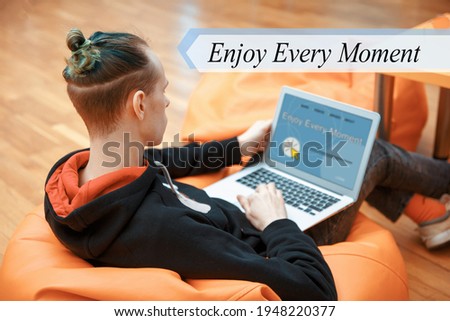 Enjoy Every Moment concept. A young man sits in an armchair and works at a computer.