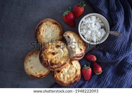 Sweet scones with cottage cheese, strawberries, blue kitchen towel and bowl with cottage on a table. Top view photo of traditional Russian pastries Vatrushka. 