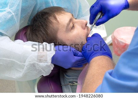 Team of dental surgeons performs surgery on teeth. in a modern clinic. Young dentist. Teamwork. Tooth doctor orthodontist surgeon doing medical operation on root canals. Stomatology office.