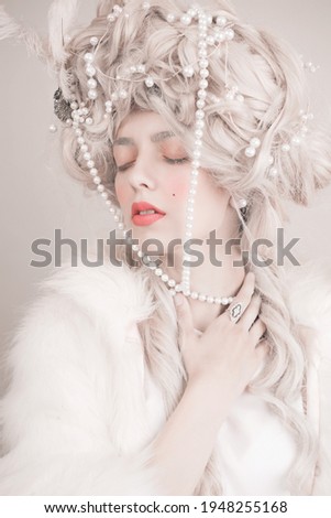Blonde with a gorgeous hairstyle rococo with strawberry in hand on a light background. The style of Marie Antoinette. Beautiful girl with white hair and pearl jewelry in her hairstyle Royalty-Free Stock Photo #1948255168