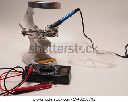 Picture of electronic repairing tools, consist of PCB holder stand, soldering iron, multimeter and protective eyeglass. Shoot on a white isolated background