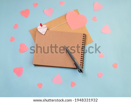 Top view on notebook and pink paper hearts on blue background with copy space