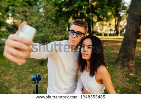 Portrait of an attractive photogenic couple taking selfies on the mobile phone. Trees and greenery on the background. Man and woman taking pictures.
