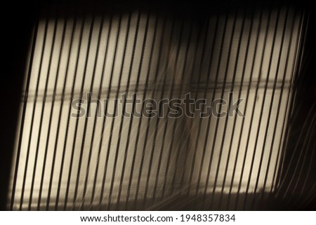 A striped shadow on the wall cast by the lowered window blinds. 