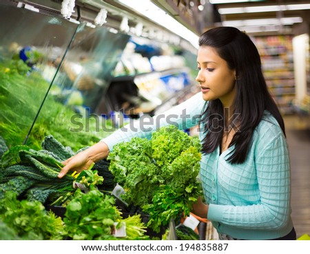 Closeup portrait, beautiful, pretty young woman in sweater picking up, choosing green leafy vegetables in grocery store Royalty-Free Stock Photo #194835887