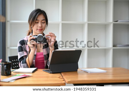 Charming female photographer or checking photo on her camera and working with computer tablet at creative office.