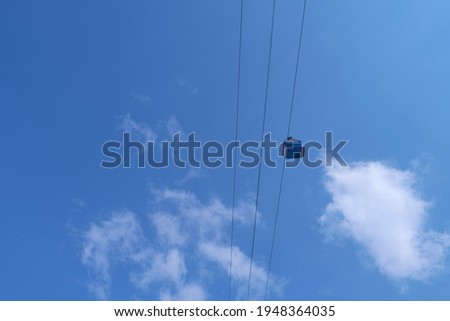 Funiculars on suspended cables move uphill against the background of a blue sky with clouds.