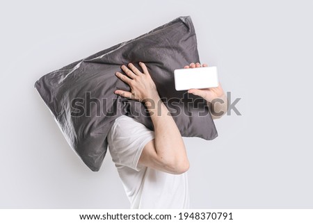 Pillow on head of young man and a smartphone in his hand on a white background. Mock up.