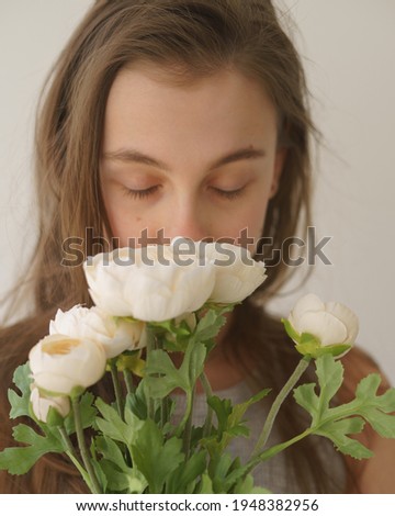 a young girl with a flower enjoys its fragrance a flower of white color a girl in a white T-shirt and with loose hair, a white knitted sweater