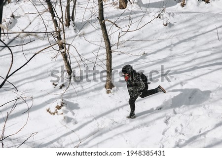 A stylish man, a wanderer, a tourist in black warm clothes with a backpack on his back runs, walks through the snowy forest, enjoying the beautiful nature. Photography, concept.