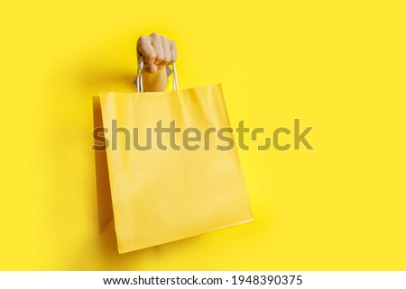 Woman hand holding yellow paper bag on yellow background . High quality photo