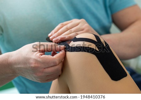 Physiotherapist applying kinesiology tape to patient knee. Royalty-Free Stock Photo #1948410376