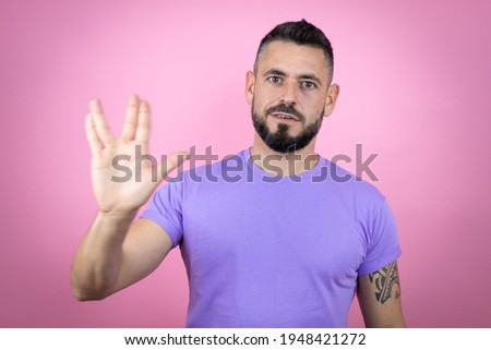 Young handsome man wearing casual t-shirt over pink background doing hand symbol