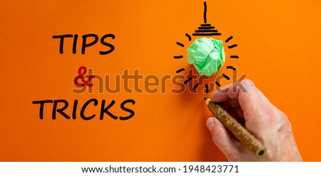 Tips and tricks symbol. Businessman writing words 'Tips and tricks', isolated on beautiful orange background. Light bulb icon. Business and Tips and tricks concept. Copy space.