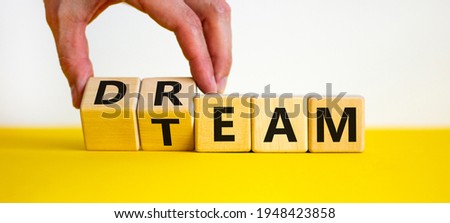 Dream team symbol. Businessman turns cubes and changes the word 'dream' to 'team'. Beautiful yellow table, white background. Business and dream team concept, copy space. Royalty-Free Stock Photo #1948423858