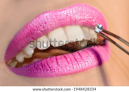 Dentist doctor select a gem or rhinestone for the patient’s teeth, Mouth close up. Shiny deep magenta-pink lip color Royalty-Free Stock Photo #1948428334