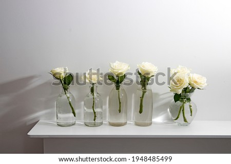 Bouquet of white roses in a glass figured vase on a white fireplace console. A faience figurine of angel as an interior decoration. Copy space. Rose White Pink O'hara.