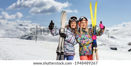 Female friends with ski and equipment gesturing a thumb up sign on a snowy mountain 