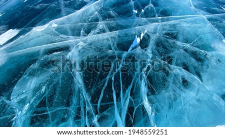 Blue transparent clear smooth ice with deep cracks. Beautiful amazing unique pattern of frozen Lake Baikal. View from above. Natural landmark of Russia.