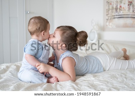 girl older sister kissing her little baby boy brother on bed at home.