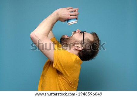 Man is tormented by thirst, he threw back head, opened mouth and pours the last drops from a paper, disposable cup. Early morning.  Royalty-Free Stock Photo #1948596049
