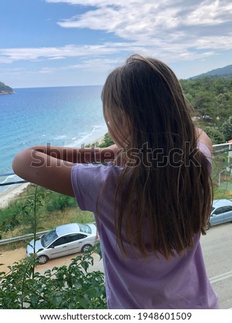 A young girl enjoys the summer sea view. A girl in pink with long hair is resting at the sea. Looking at the beautiful blue sea.