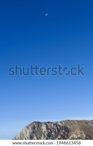 Minimal mountain landscape with mountain under clear blue sky with moon.