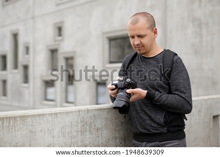 portrait of male photographer or videographer watching video or photos on his camera over concrete building background