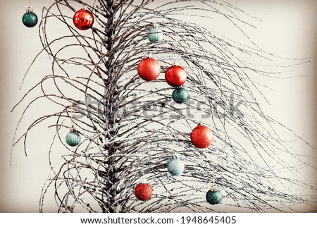 Bare tree branches with red and green Christmas baubles hanging against a white background