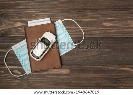 Top view photo of car model on leather passport cover with vaccination card and medical face mask on isolated wooden table background with copyspace