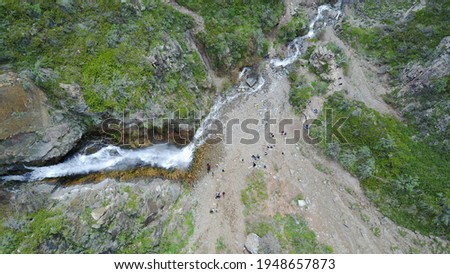 Top view of the waterfall among the rocks. Highest waterfall, and longest river. Grass and trees grow on the rock. A group of people can be seen below. Outdoor recreation. Mountainous area. Royalty-Free Stock Photo #1948657873