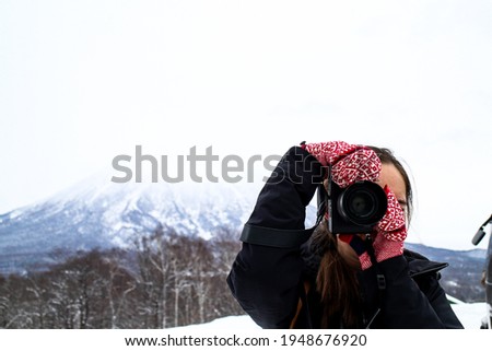 Girl wearing black jacket and red and white patterned gloves taking photograph. Scenic mountain in the background. Niseko, Hokkaido, Japan
