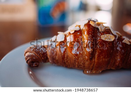 appetizing croissant with almond petals and syrup on a white plate on a wooden table. image with selective focus