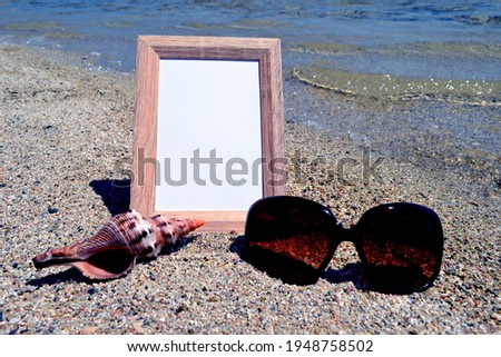 Topic: "Photos from the rest". Wooden frame for photos on the background of the sea surf. Pebbles, seashell, sunglasses.
