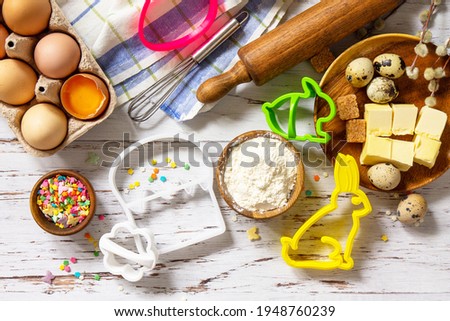 Baking or cooking background frame. Ingredients, kitchen items for Easter festive baking. Kitchen utensils, flour, brown sugar, eggs, butter, confetti on rustic kitchen table. Flat lay. Top view.