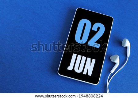 June 2. 2 st day of the month, calendar date. Smartphone and white headphones on a blue background. Place for your text. Springtime month, day of the year concept.