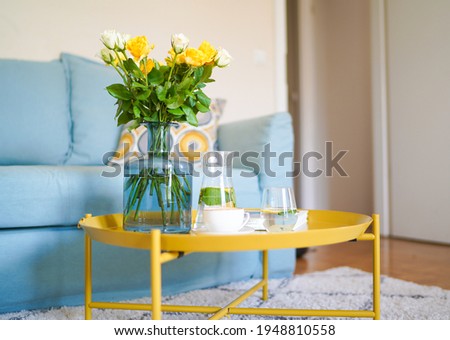 Cup of coffee with milk on the yellow coffee table, lemonade and yellow roses bouquet on the background. Cozy home interior. Yellow colour in interrior
