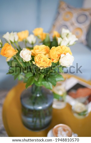 Cup of coffee with milk on the yellow coffee table, lemonade and yellow roses bouquet on the background. Cozy home interior. Yellow colour in interrior