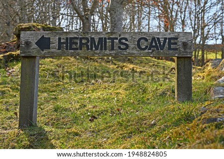 Wooden sign for Hermits Cave with arrow, blurred rural background. Taken in Perthshire, Scotland near Falls of Acharn