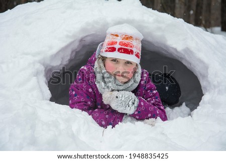 Girl in winter clothes playing at a snow hole