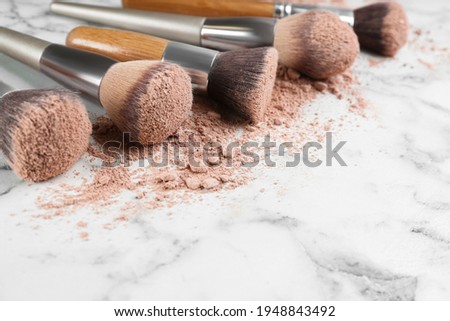 Different makeup brushes with crushed cosmetic product on white marble table, closeup. Space for text