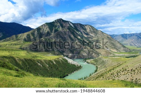 The Katun River in Altai in a high-mountain valley, in the background there are high rocky mountains of the ridge, near the river there are high banks, summer, sunny